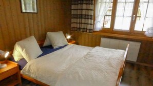A wooden-paneled room with a bed, a nightstand, a window with curtains, and a radiator. - Chalet Doris by Interhome (Grindelwald)