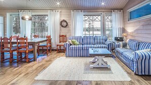 Un interior de cabaña acogedor con comedor, un conjunto de sofás y una televisión.