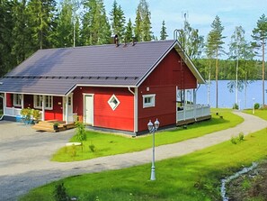A red wooden house with a porch, a small garden, and a lake in the background. - Villa kantri by Interhome (Multia)
