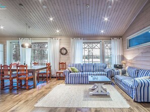 A cozy room with a wooden ceiling, a striped sofa set, a dining table with chairs, and a large window. - Villa kantri by Interhome (Multia)