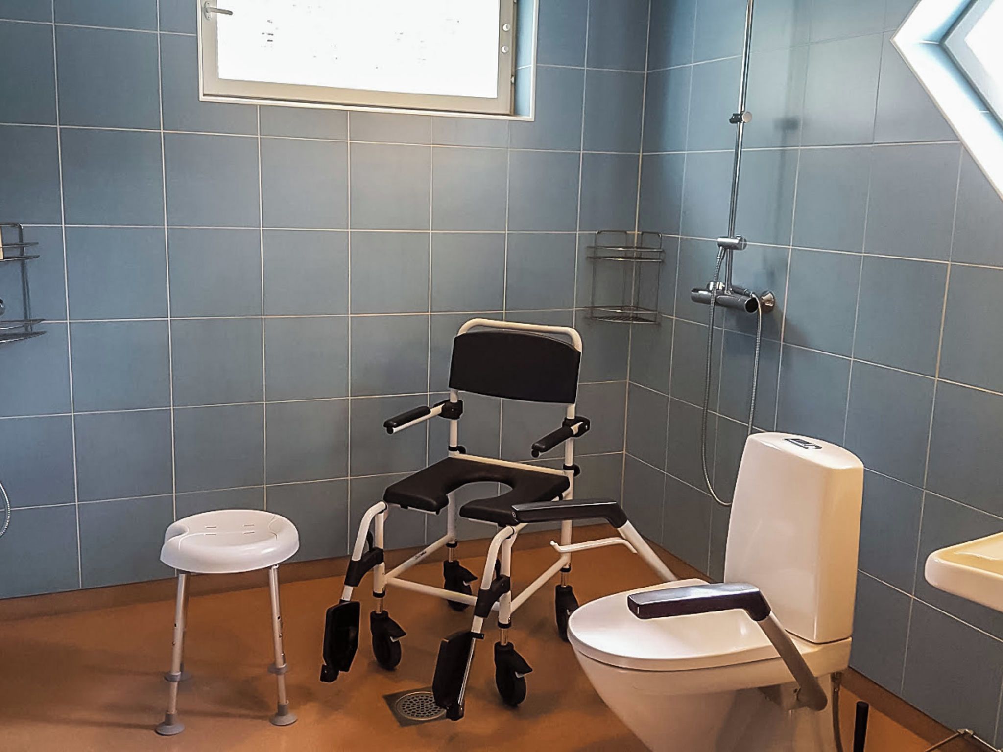 Ein Badezimmer mit Rollstuhl, Toilette und einem kleinen Hocker.