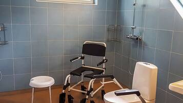 Ein Badezimmer mit Rollstuhl, Toilette und einem kleinen Hocker.