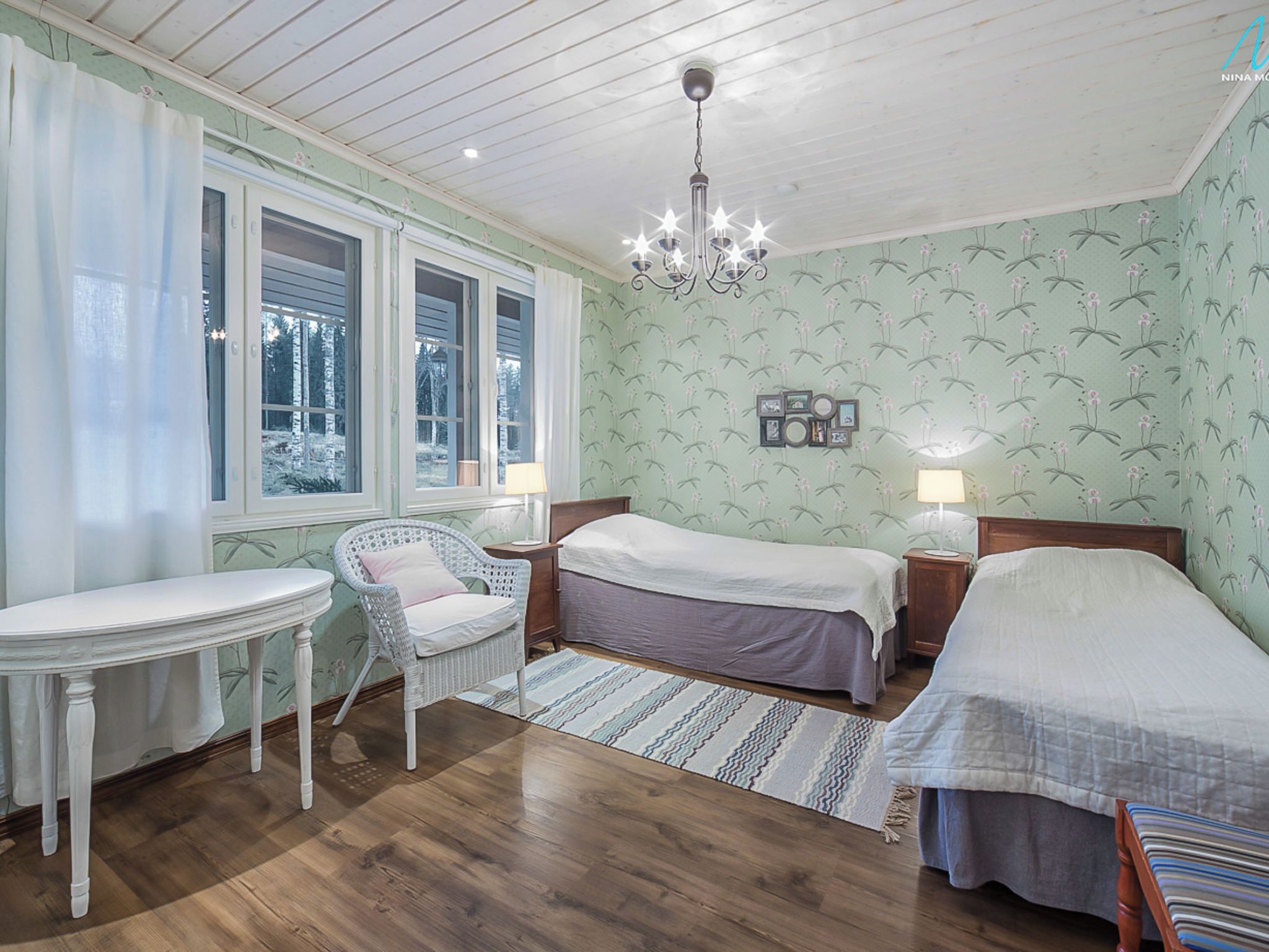 Een slaapkamer met twee bedden, een klein tafeltje, een stoel en een kroonluchter.