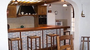 Eine Küche mit Ziegelrückwand, Holzbarhocker und Holzbalkendecke.