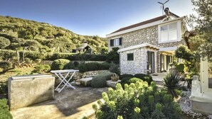 Une maison en pierre avec une petite dépendance attenante, entourée d’une végétation luxuriante et d’un paysage vallonné.