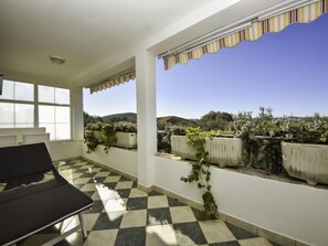 Une pièce baignée de lumière, avec un sol à carreaux, une chaise noire et une vue sur des plantes en pot et des collines à l’extérieur.