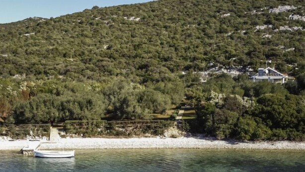 Un paysage côtier avec un bateau sur l’eau, une côte rocheuse et un bâtiment en arrière-plan.