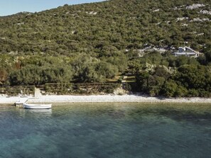 Un paysage côtier avec un bateau sur l’eau, une côte rocheuse et un bâtiment en arrière-plan.