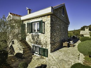 Une maison en pierre avec un escalier en pierre menant à l’entrée, un petit patio avec des meubles d’extérieur et un ciel d’un bleu limpide.