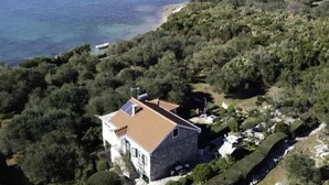 Une maison en pierre avec un toit de tuiles, entourée d’une végétation luxuriante et bordée d’un plan d’eau.