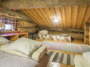 Une chambre mansardée chaleureuse, avec un plafond en pente, des poutres apparentes et un lit simple agrémenté d’oreillers.