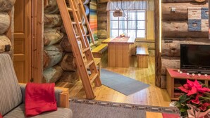 L’intérieur d’un chalet confortable en bois, avec un escalier en bois, un coin repas et un téléviseur.