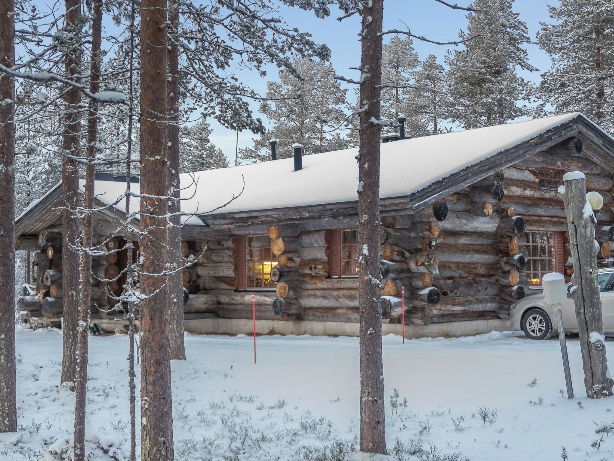 A log cabin with a snow-covered roof, surrounded by trees.