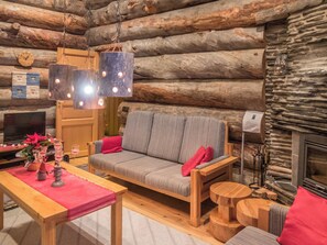 A cozy log cabin interior with a sofa, wooden table, and a fireplace.
