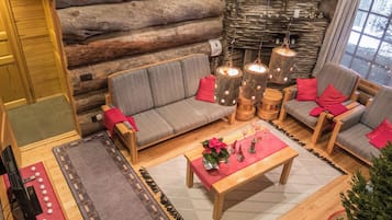 Interno di una baita di legno con un divano, poltrone, un tavolino da caffè e un camino.
