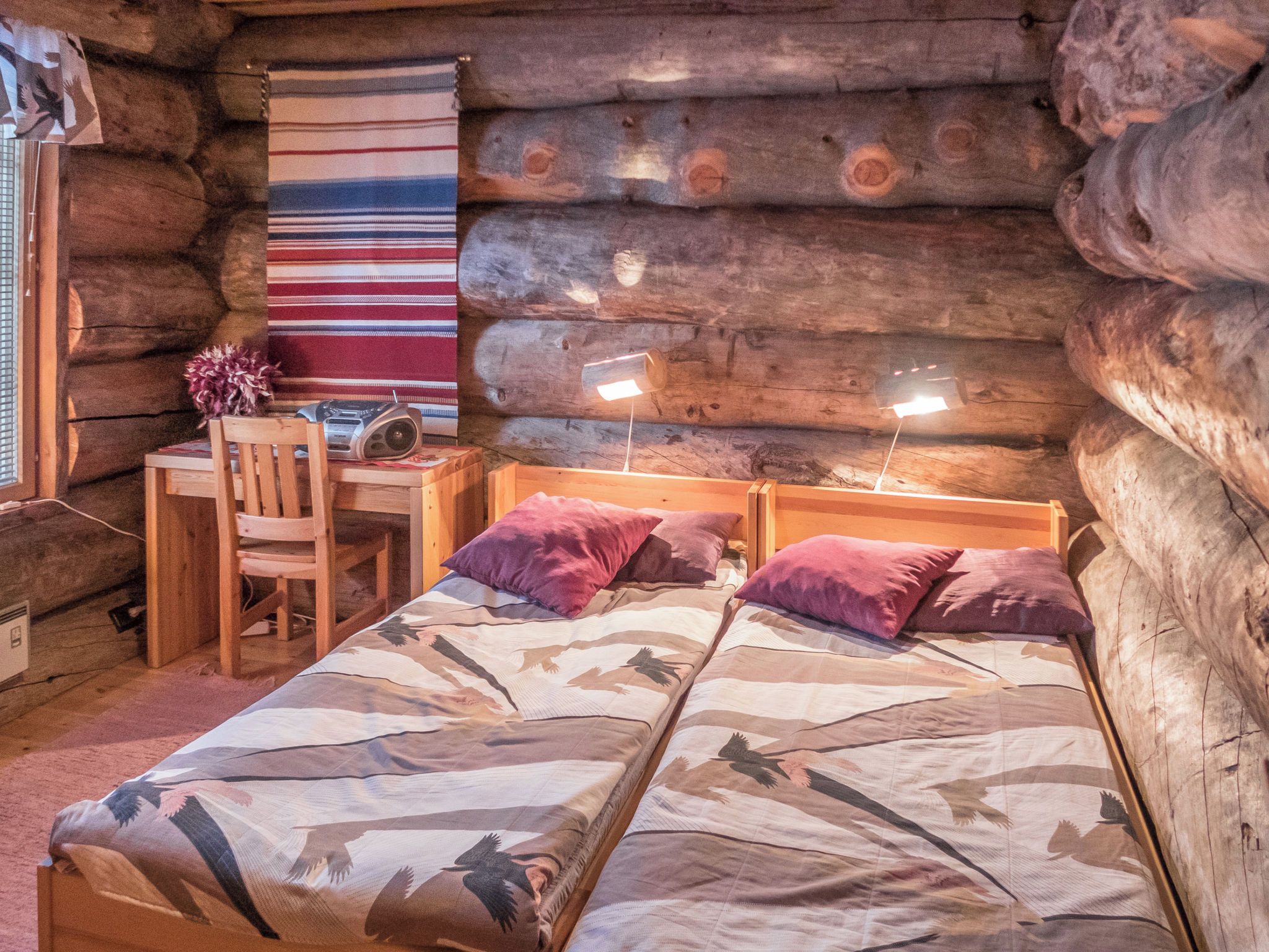 A log cabin room with a bed, desk, chair, and a radio.
