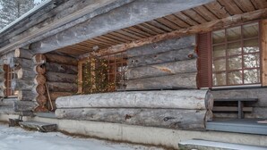 Une cabane en rondins avec un porche en bois, une fenêtre avec des volets et un sol recouvert de neige.