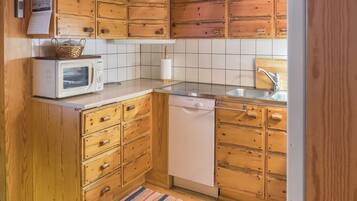 Ett kompakt kök med träskåp, en mikrovågsugn, en diskmaskin och en kakelbeklädd vägg bakom arbetsbänken.