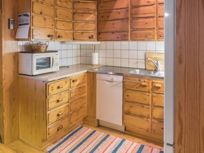 Cocina compacta con muebles de madera, microondas, lavavajillas y salpicadero de azulejos.
