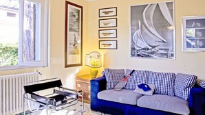 Une pièce avec un canapé bleu, un fauteuil noir, un radiateur et des œuvres d’art encadrées accrochées au mur.