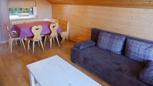Una habitación acogedora con techo de madera, una mesa de comedor con sillas y un sofá con cojines a cuadros.
