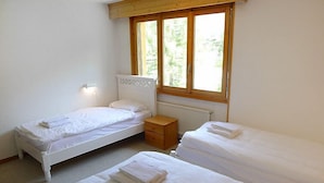 Un dormitorio con dos camas individuales, una mesita de noche de madera y una ventana con vistas a zonas verdes.