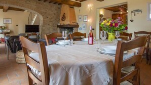 A dining area with a table set for four, wooden chairs, a fireplace, and a TV in the background.