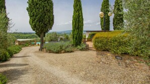 A gravel driveway leading to a building with a stone wall and a pergola.