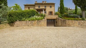 A stone villa with a central courtyard, surrounded by lush greenery and tall trees.
