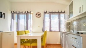 Een compacte keuken met een eethoek, voorzien van een kleine koelkast, een witte tafel met gele stoelen en een klok aan de muur.