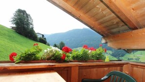 Une table et une chaise en bois, dans une pièce offrant une vue sur des collines verdoyantes et des montagnes.