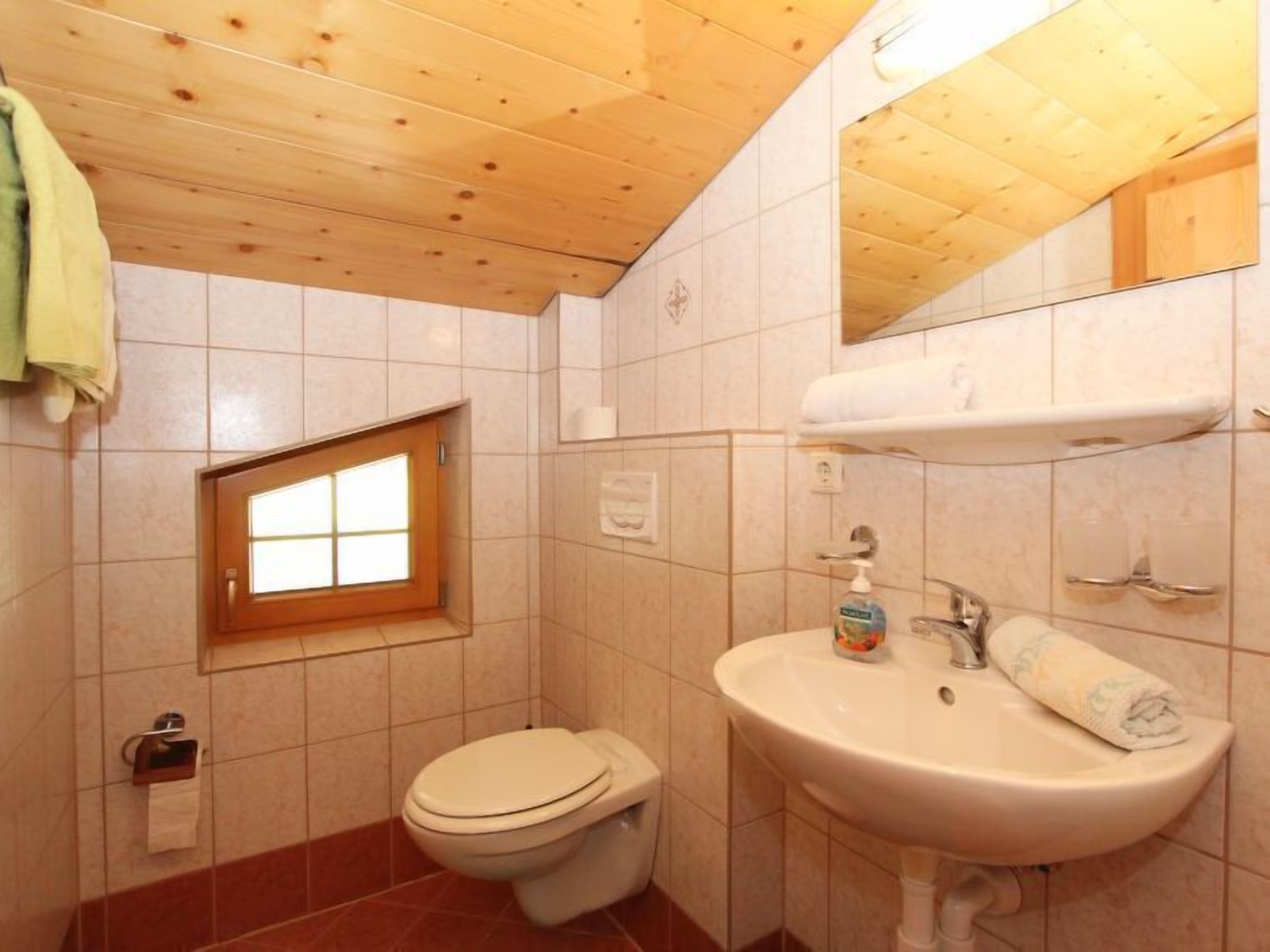 Un baño con techo de madera, una ventana, inodoro, lavabo y toallero.