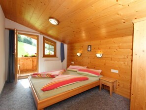 A wooden-paneled bedroom with two beds, a small bedside table, and a window with curtains.
