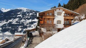 Un immeuble en bois à plusieurs étages, doté de balcons, qui se dresse sur fond de montagnes enneigées et d’un ciel dégagé.