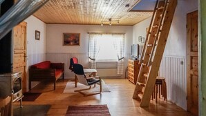 Et hyggeligt loftsværelse med trægulv, en gyngestol, sofa, fjernsyn og en stige.