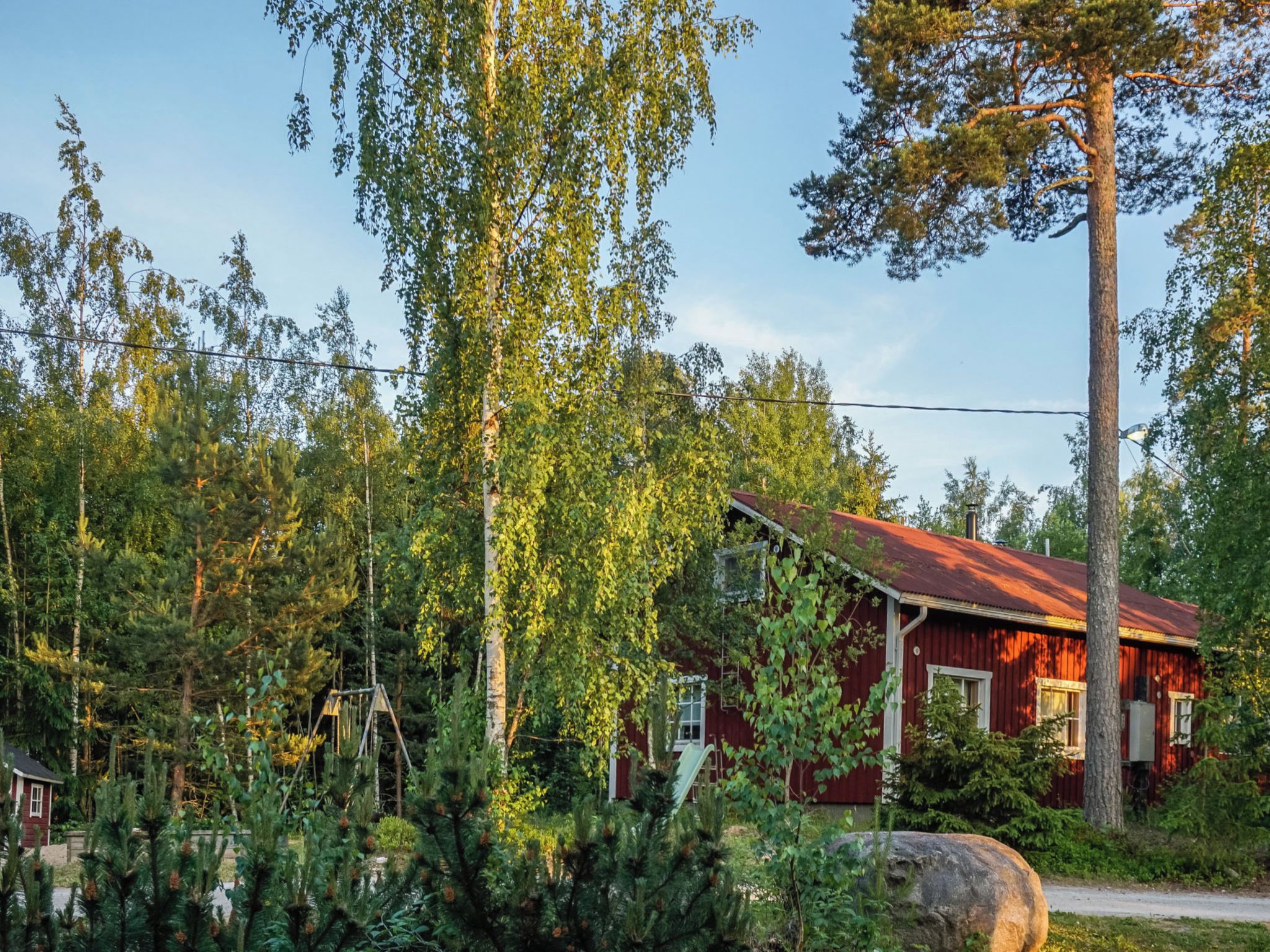 A red wooden cabin surrounded by dense forest, with a clear sky above.