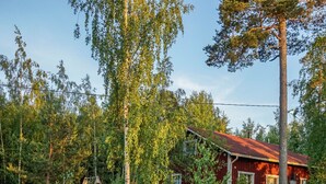 En rød træhytte omgivet af tæt skov.