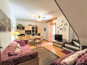 A living room with a sofa, a dining table with chairs, a TV, and a staircase.