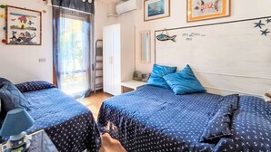 A bedroom with two beds, a ceiling fan, a window with curtains, and wall decorations including framed pictures and a fish mural. - Barracuda by Interhome (Grosseto)