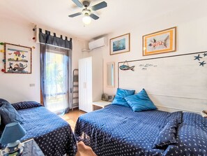 A bedroom with two beds, a ceiling fan, a window with curtains, and wall decorations including framed pictures and a fish mural.