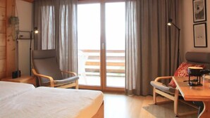 A room with a bed, two chairs, a table with a kettle, and a balcony with curtains. - Le Bristol B36 by Interhome (Villars)