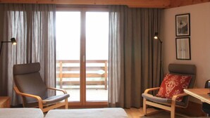 A room with a bed, two chairs, a table, a lamp, and a large sliding glass door leading to an outdoor balcony. - Le Bristol B36 by Interhome (Villars)