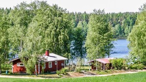 Punainen mökki, jonka katto on tehty metallista, ja jonka ympärillä on vehreä niitty ja tiheä metsä.