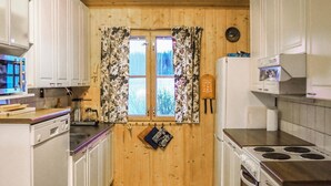 Pieni, käytännöllinen keittiö, jonka seinät ovat puuta, kaapit valkoisia, ja siellä on liesi sekä jääkaappi.