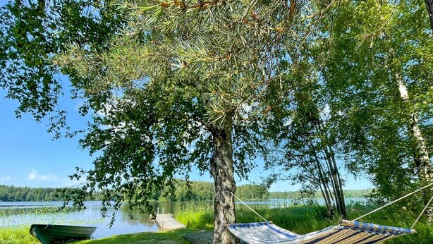 Riippumatto on kiinnitetty puuhun järven rannalla, ja lähellä on laiturissa oleva vene.