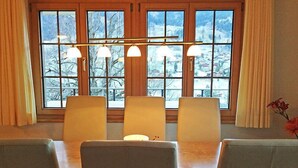 A dining area with a wooden table and four chairs, a window with curtains, and a chandelier. - Chalet Perle by Interhome (Grindelwald)