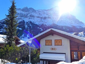 Un chalet de montagne avec un toit enneigé, des volets en bois et une enseigne indiquant « Bergele ».