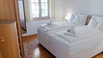 Une chambre d’hôtel avec une armoire en bois, un lit double avec une literie blanche, une fenêtre avec des rideaux et un plancher en parquet.