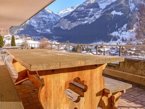 A wooden table with a view of snow-covered mountains and a town in the background. - Chalet Perle by Interhome (Grindelwald)