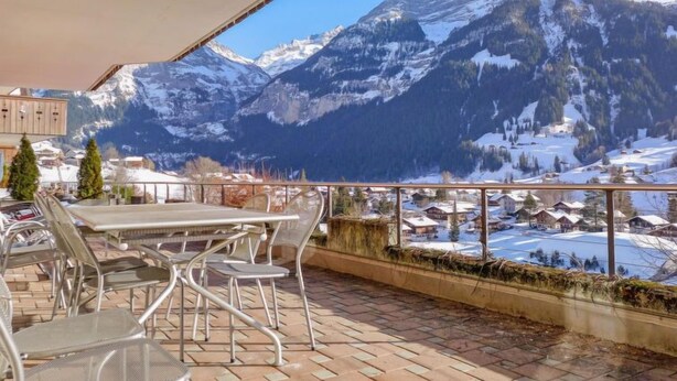 A terrace with metal chairs and tables, overlooking a snowy mountain landscape with a village below. - Chalet Perle by Interhome (Grindelwald)